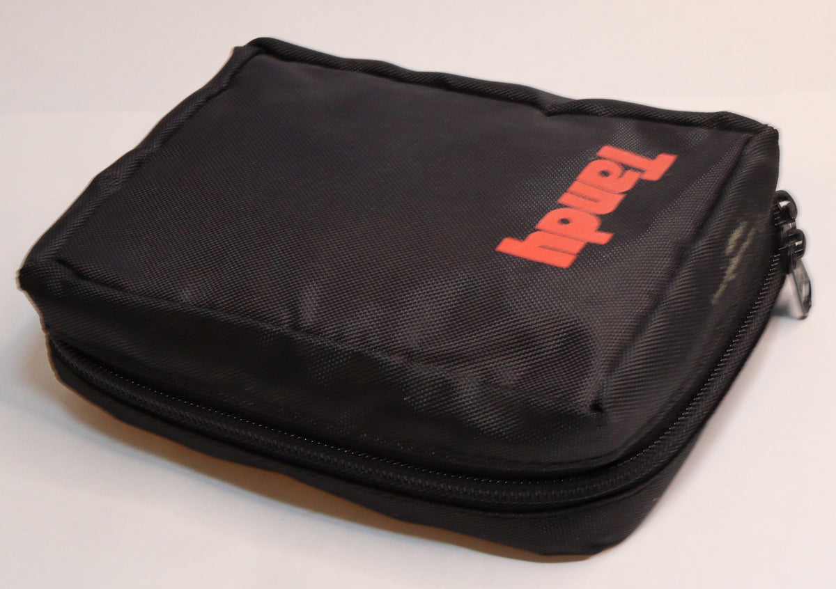 A black zippered fabric pouch with a red 'Tandab' logo, placed on a white surface next to a blue tool tray containing pens and small tools.